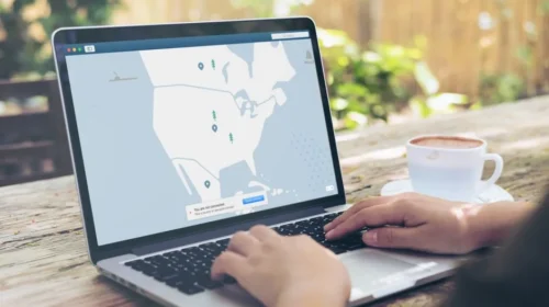 Hands typing on a laptop outdoors with a VPN interface displayed, next to a cup of coffee.