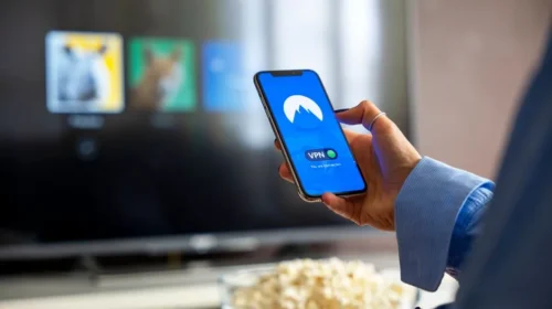Person using VPN on smartphone while watching smart TV at home.